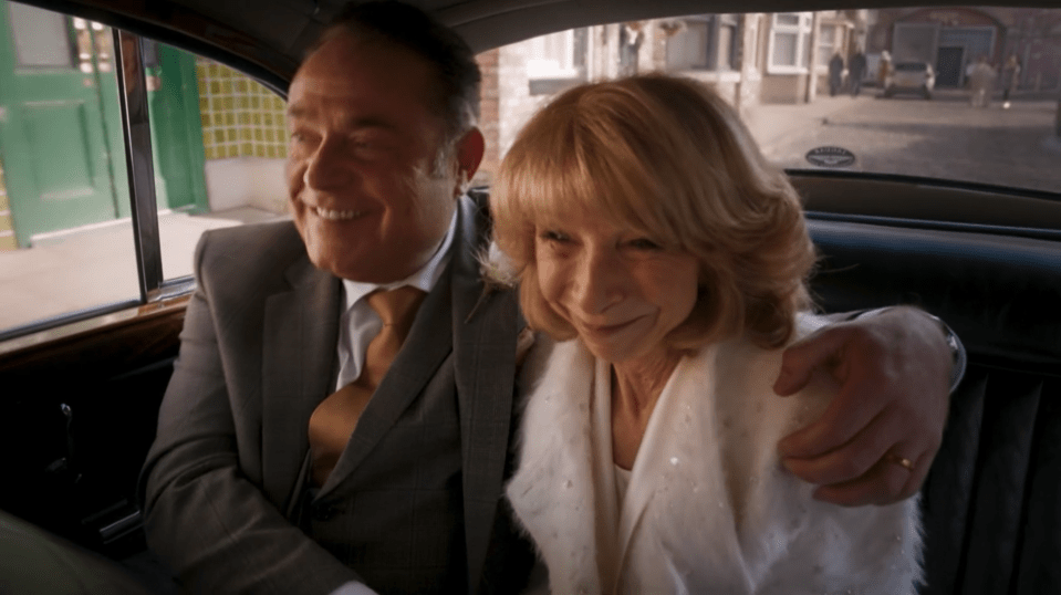 A smiling couple sits in the back of a car.