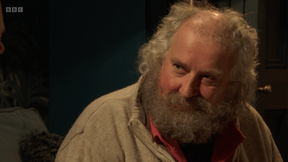 Close-up of a man with a long gray beard, wearing a beige cardigan.