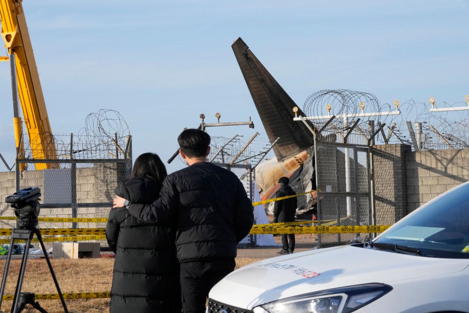 Mourners watch the site of a plane fire from outside of Muan International Airport