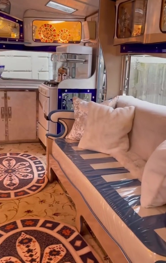 Interior view of a luxurious caravan, showing a sofa, rugs, and kitchen area.