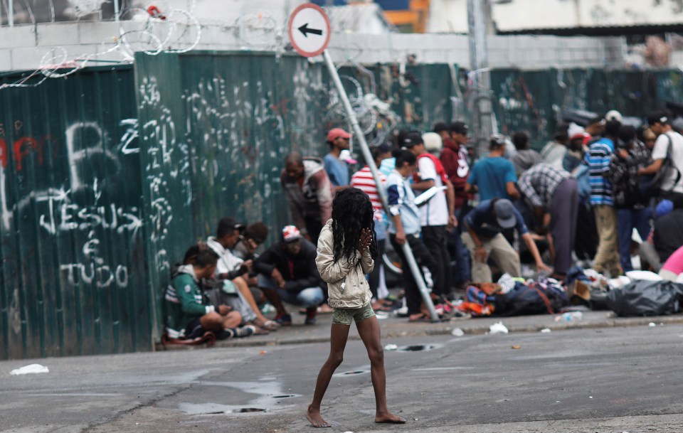 A young woman walks barefoot in Cracolandia, a drug-ridden abandoned site in Sao Paulo, Brazil, surrounded by other people.