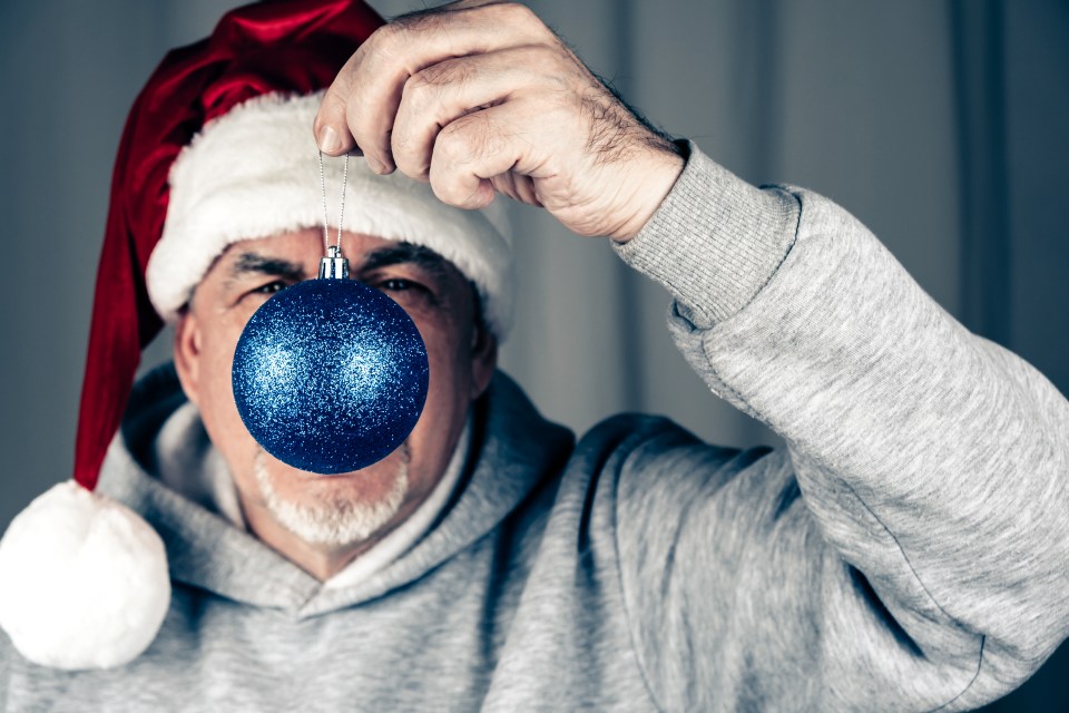 Man in Santa hat holding a blue Christmas ornament.