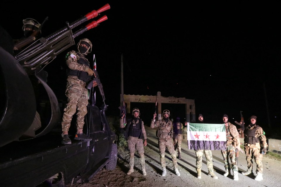 Anti-government fighters pose for a picture at the entrance of the northern Syrian town of Tal Rifaat