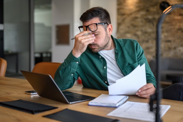 Stressed financial advisor reviewing documents at his desk.