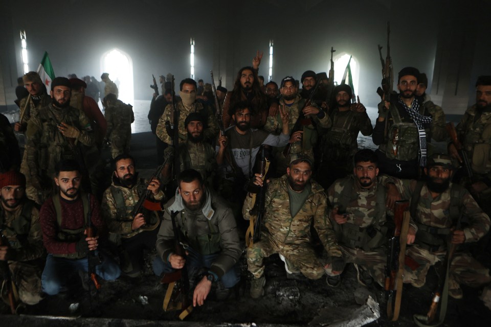 Armed rebel fighters pose next to the charred grave