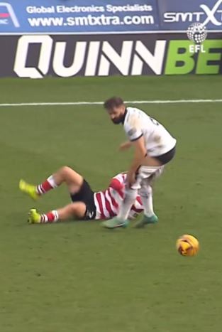 Soccer player falls to the ground as another player stands over him.