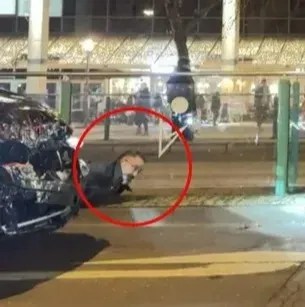 Person lying on the ground near a damaged car.