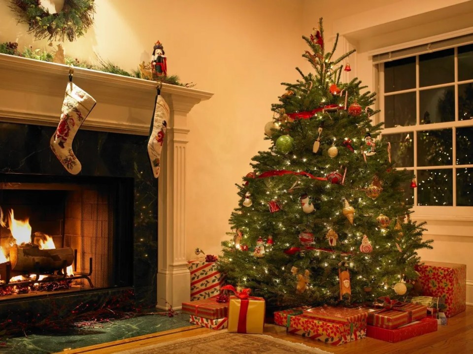 Decorated Christmas tree in living room with fireplace and presents.