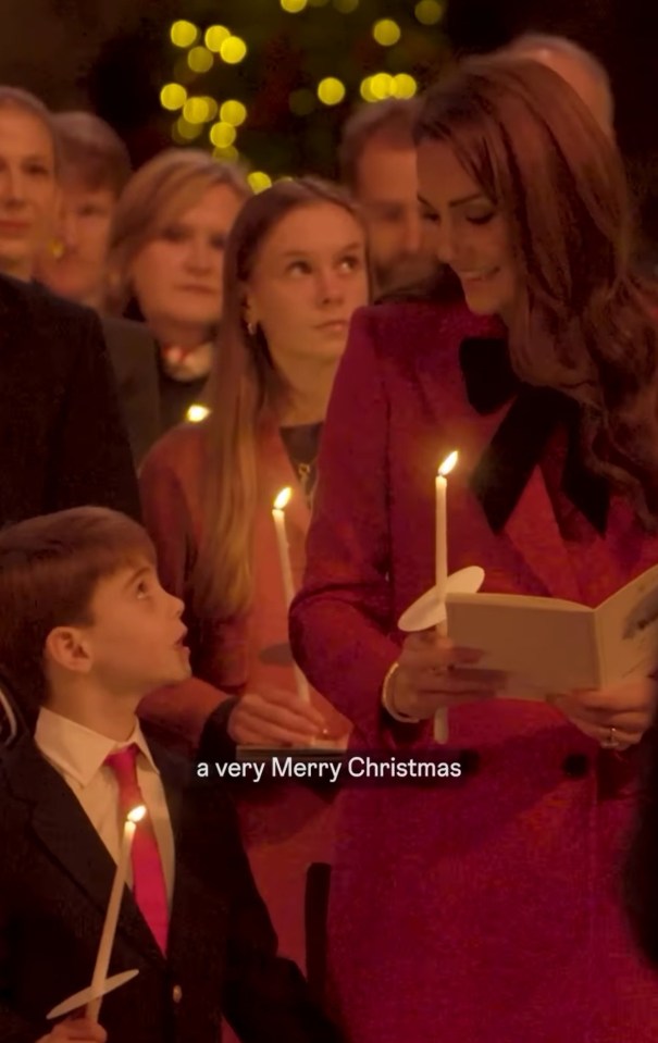 A woman in a red dress holds a candle and a book, while a young boy holds a candle next to her.  A Christmas tree is in the background.