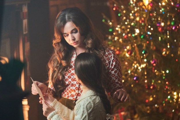 A woman and a girl look at a card together in front of a Christmas tree.