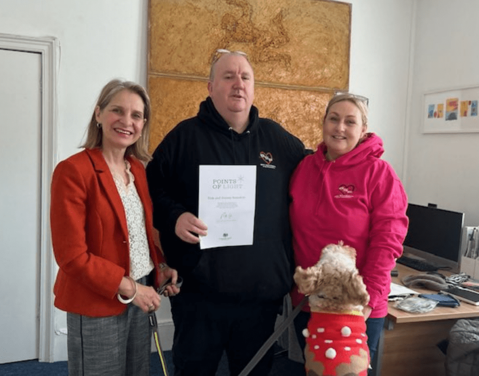 Three people and a dog pose for a photo; one person holds a Points of Light award certificate.