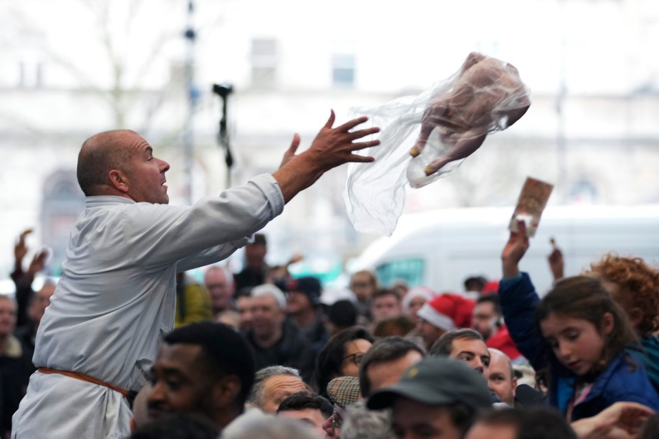 A butcher throws a turkey to customers at a meat auction.