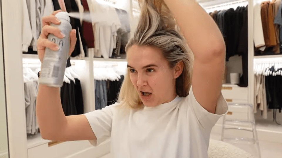 Woman spraying hairspray in a walk-in closet.