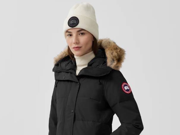 Woman in black Canada Goose parka and cream knit hat.