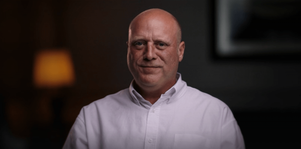 Headshot of a middle-aged, bald man in a light-colored collared shirt.