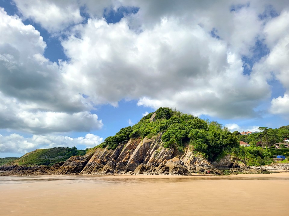 Caswell Bay beach in Wales, with a rocky cliff and cloudy sky.