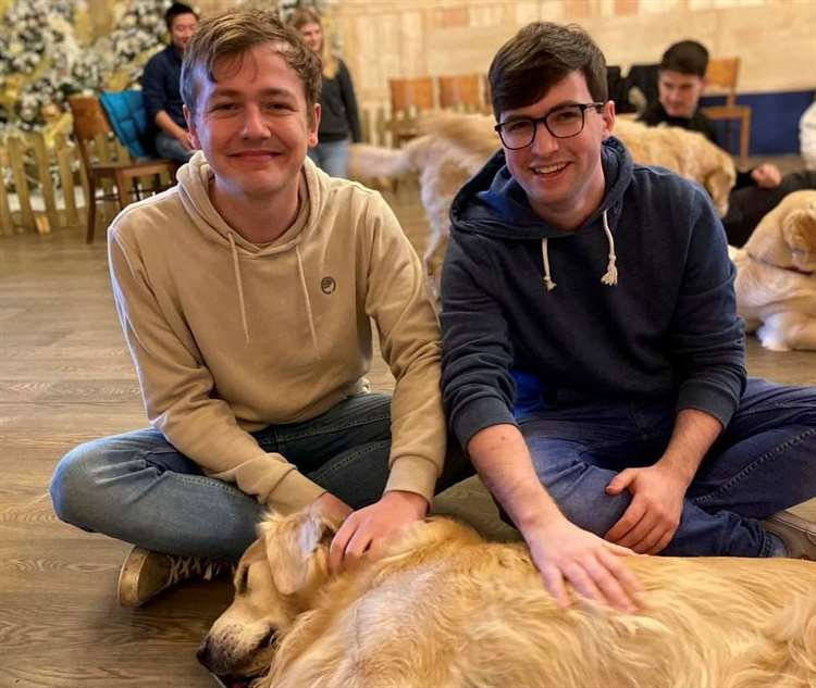 Two young men petting a golden retriever.