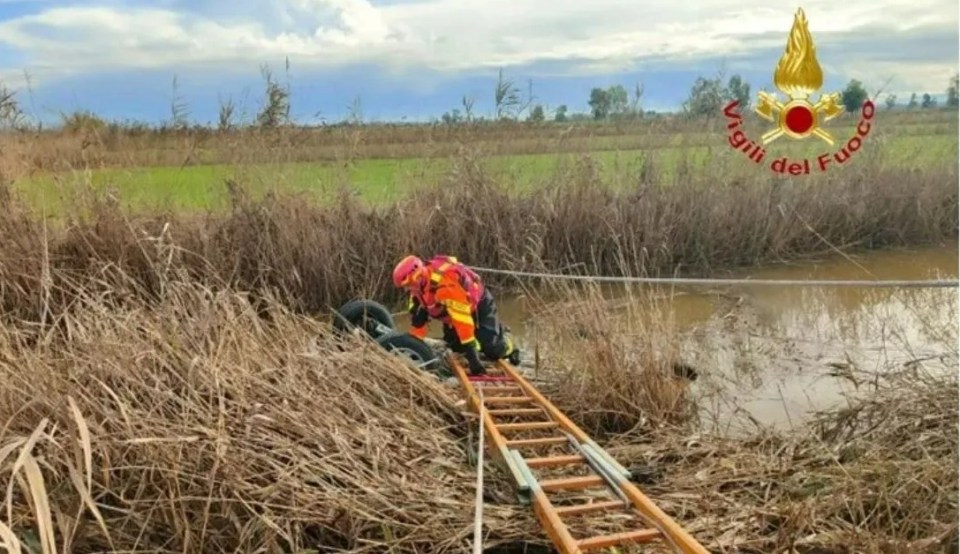 A firefighter uses an extended ladder to reach the overturned car in the canal in southern Italy