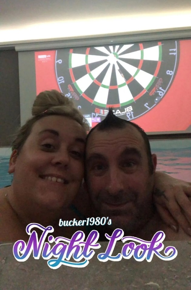 Couple selfie in a hot tub with a dartboard projected on the wall.