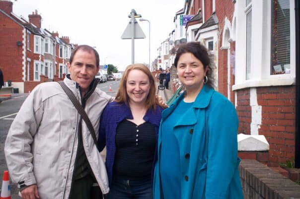 Three people stand on a street outside a row of houses.