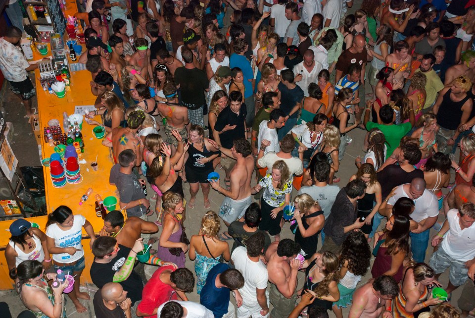 A large crowd of people dancing at a beach party at night.