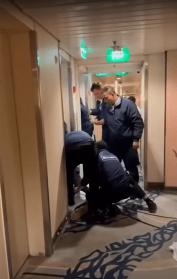 Cruise ship security personnel attending to a passenger on the floor of a hallway.