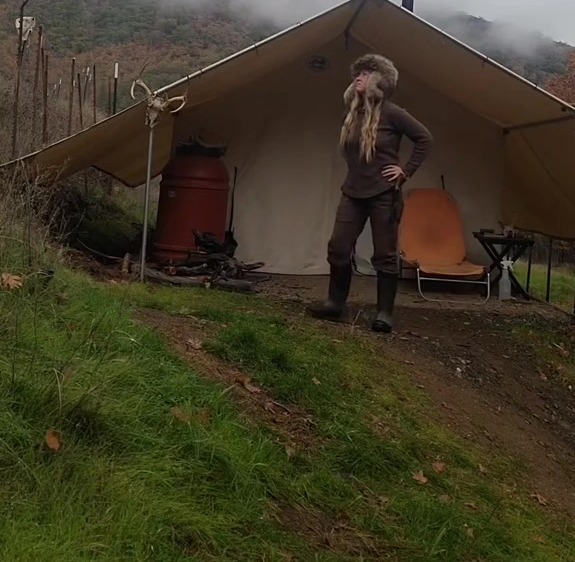 Woman standing outside her wall tent.