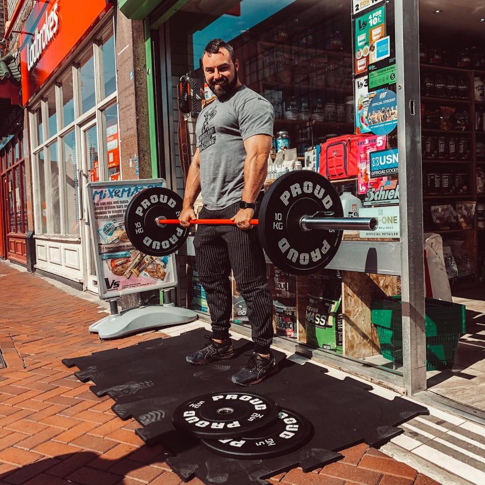 Bodybuilder Karol Olender posing with weights outside his fitness business.