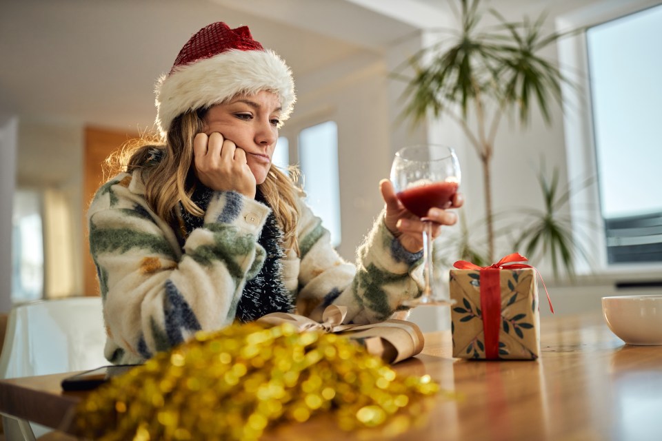 Sad woman in Santa hat drinking wine alone on Christmas.