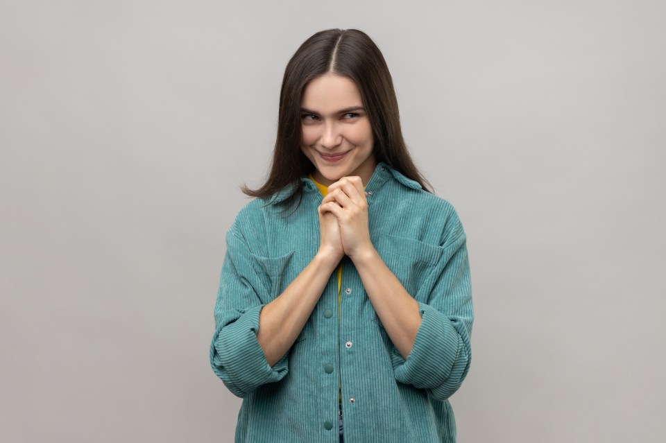 Young woman with a sly smile, clasping her hands.