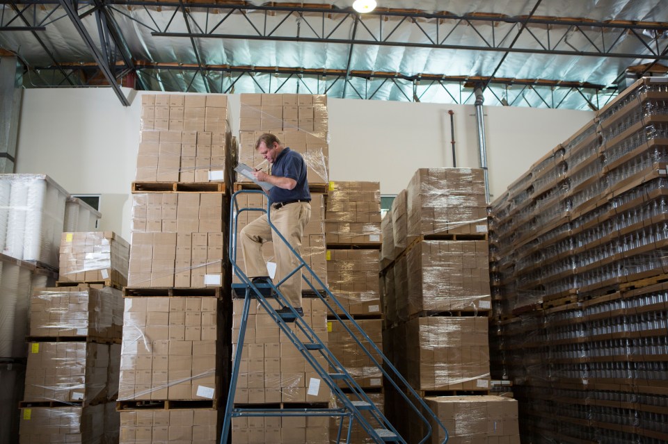 Man on ladder taking inventory in warehouse.