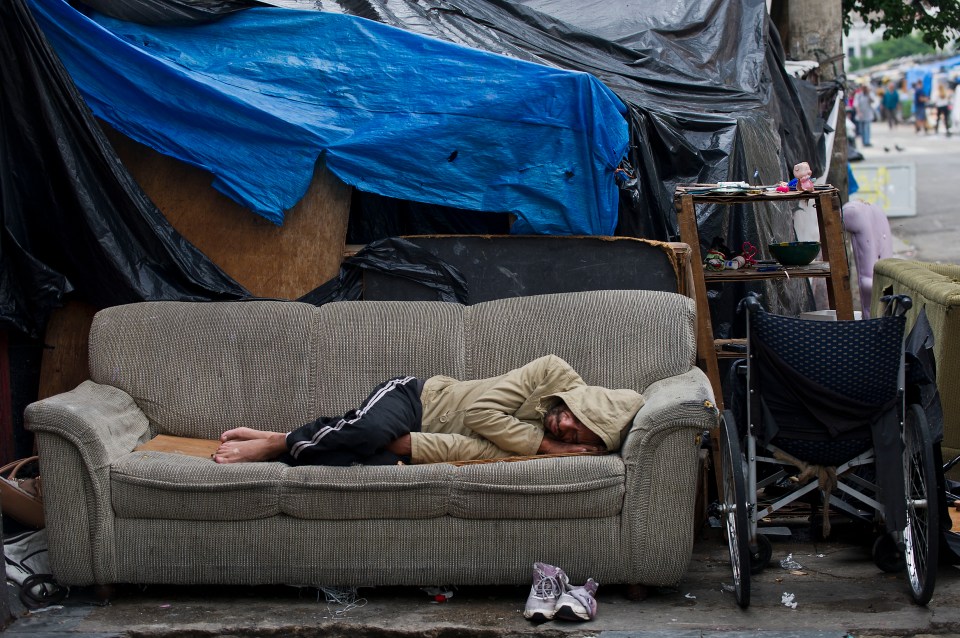 A person sleeping on a couch outdoors in a makeshift shelter.