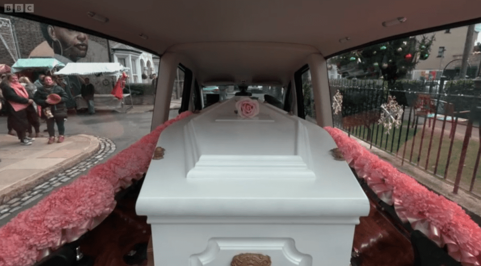 A white coffin with a pink rose inside a hearse.