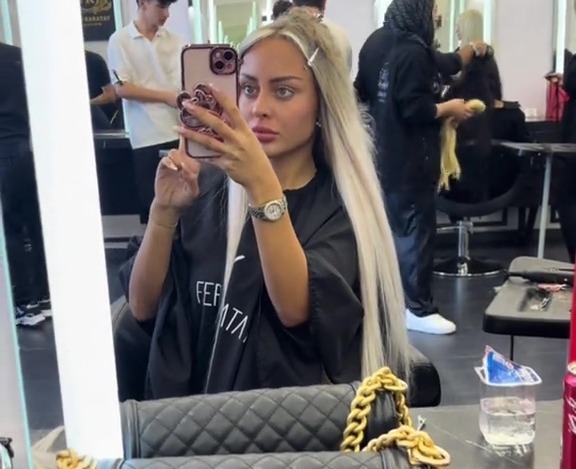 Woman in a hair salon taking a selfie, showing off her new hair and Chanel bag.