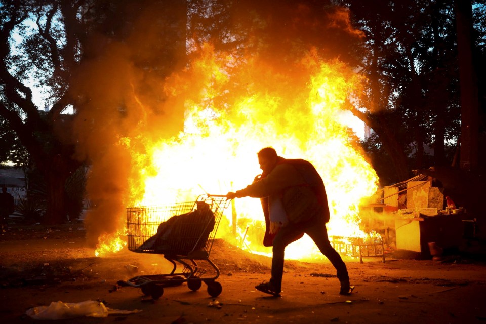 A person pushes a shopping cart away from a large fire during a police operation in Cracolandia, Sao Paulo, Brazil.