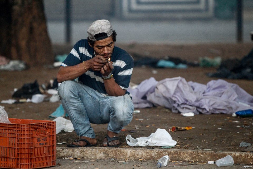 A person smokes crack cocaine in a littered area.