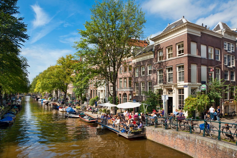 Amsterdam canal with people sitting outside at a cafe.