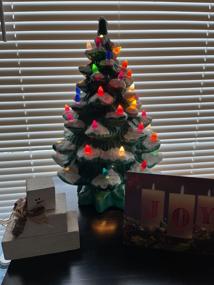 Lit ceramic Christmas tree with colorful lights, next to a wooden snowman and a Christmas card.