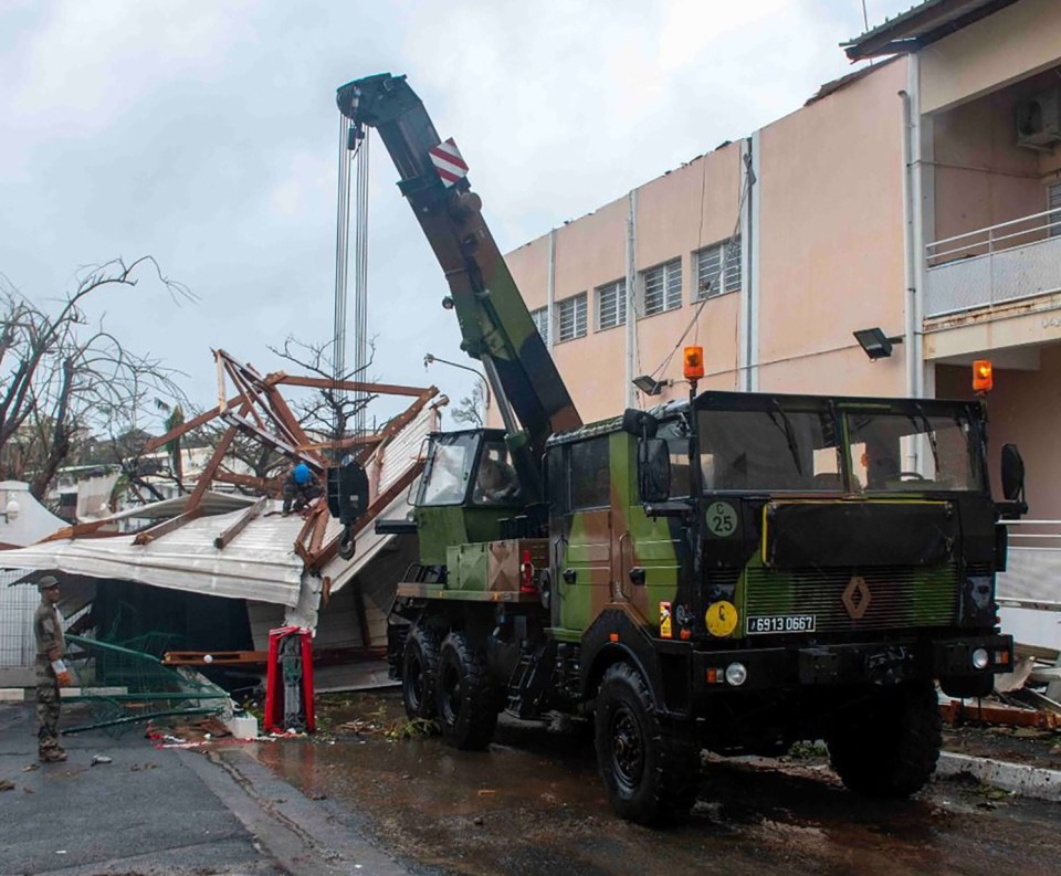 Military trucks work to remove piles of debris from the streets of the French territory