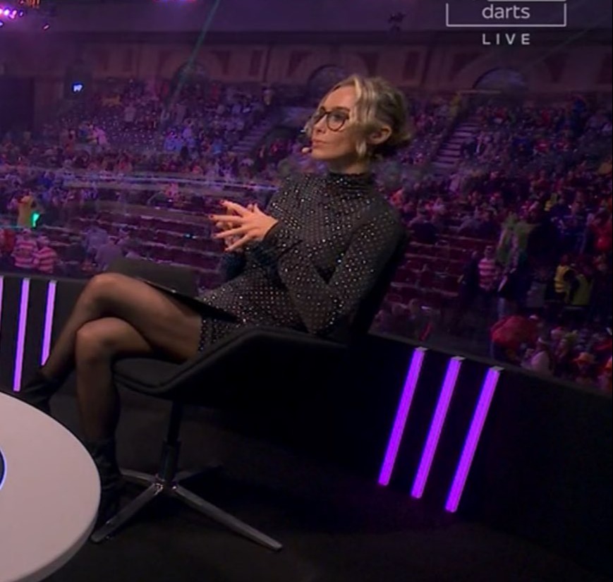 A woman sits in a chair on a darts broadcast, talking.