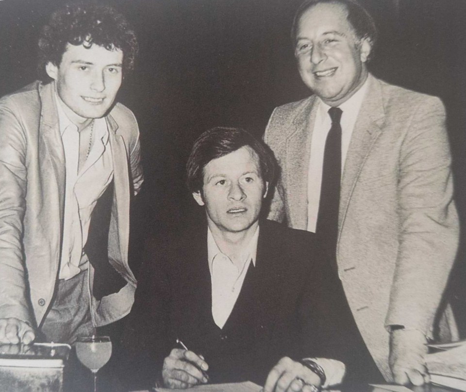 Three men in suits; one is signing a document.