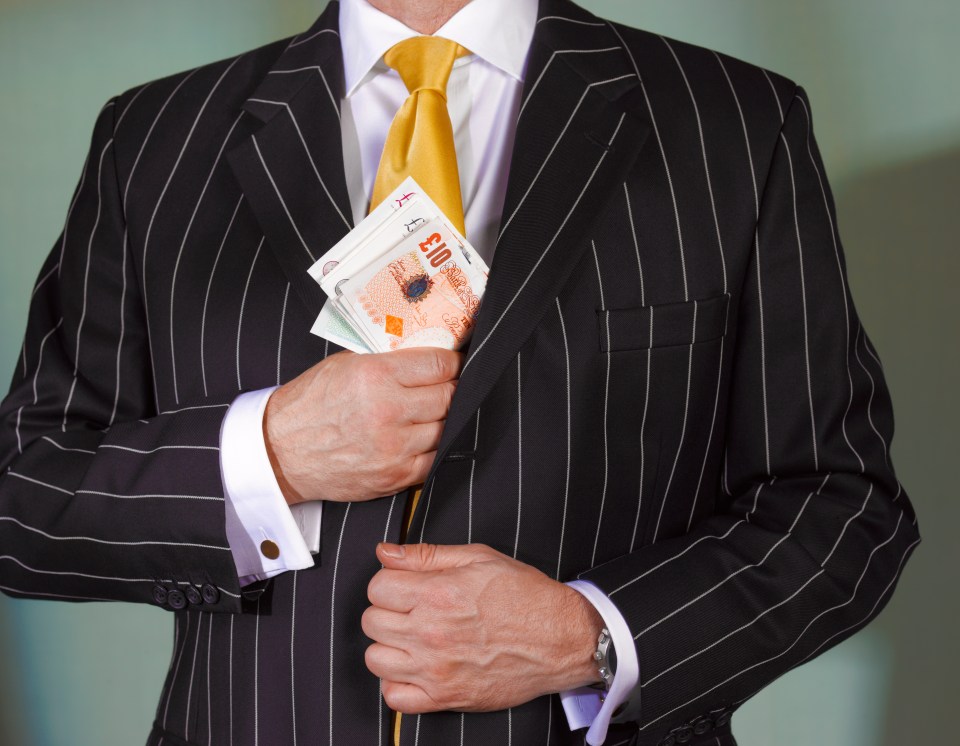 A man in a pinstripe suit concealing British banknotes in his jacket pocket.