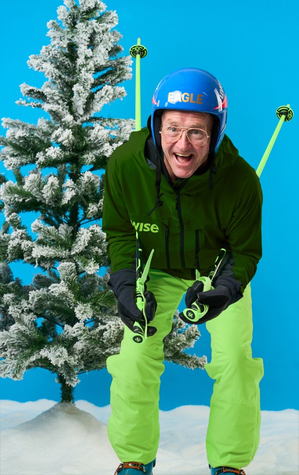 Eddie "The Eagle" Edwards in a Wise-branded ski suit, holding skis and poles, in front of a snowy Christmas tree.