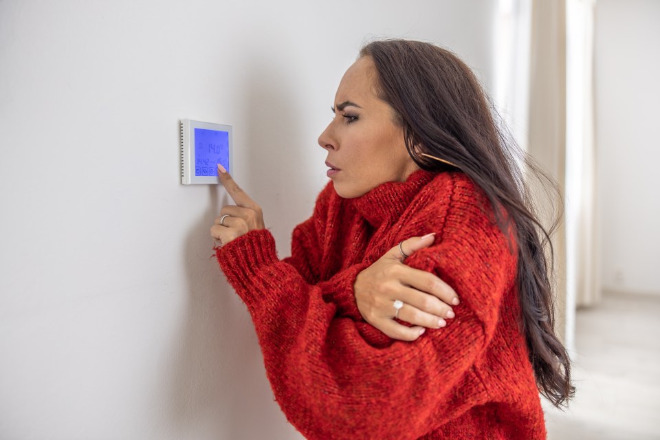 Woman in red sweater raises thermostat temperature during energy crisis.