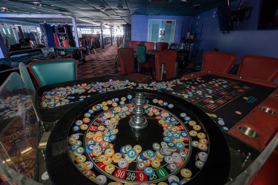 Abandoned casino interior with roulette wheel and gaming tables strewn with chips.