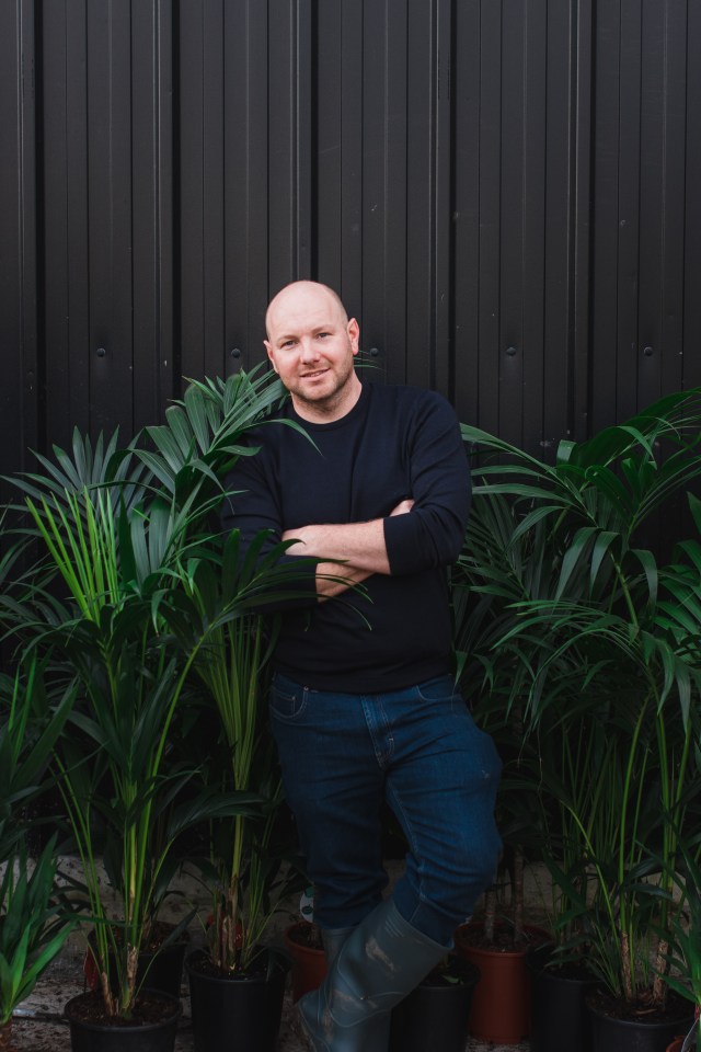 A gardener stands among potted plants.