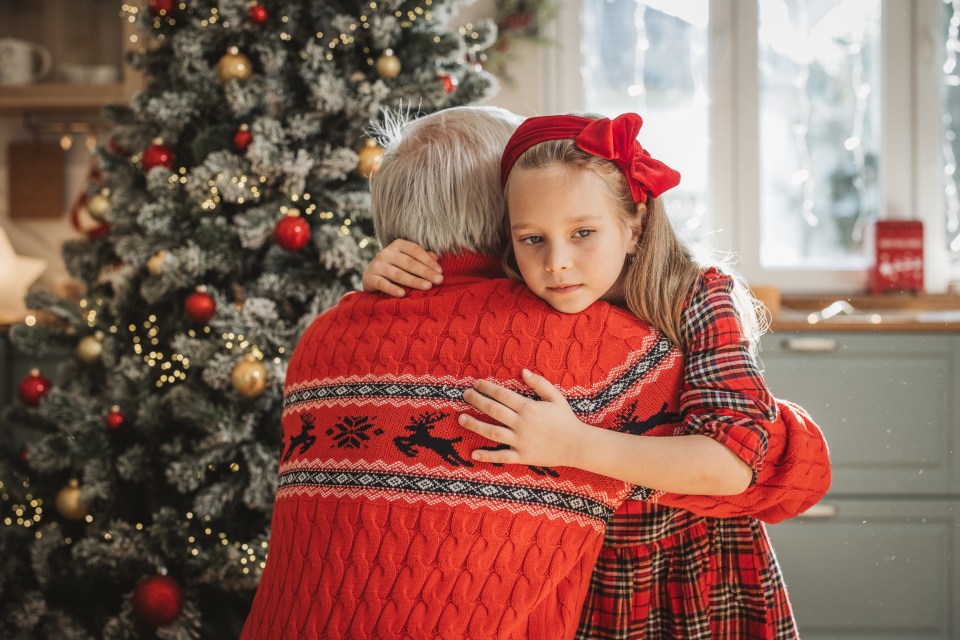 Grandfather and granddaughter hugging in front of a Christmas tree.