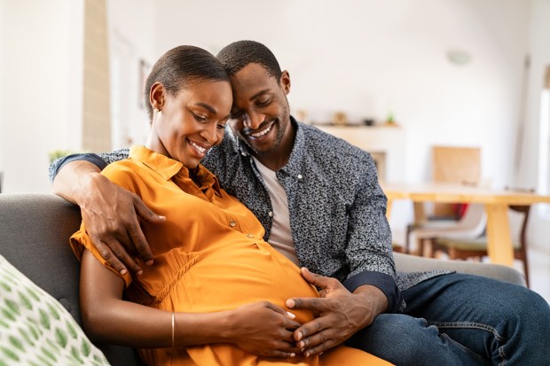 Happy African-American couple embracing while the woman holds her pregnant belly.