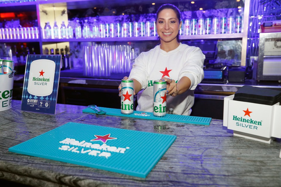 Bartender presenting Heineken Silver beer cans at a bar.