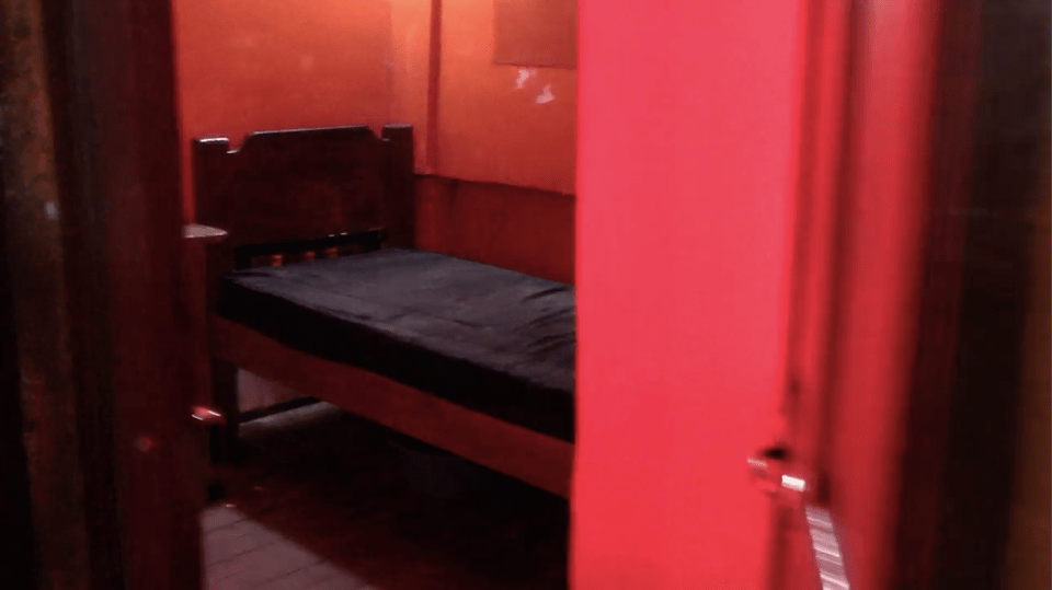 A small bed in a cramped, red-walled room.